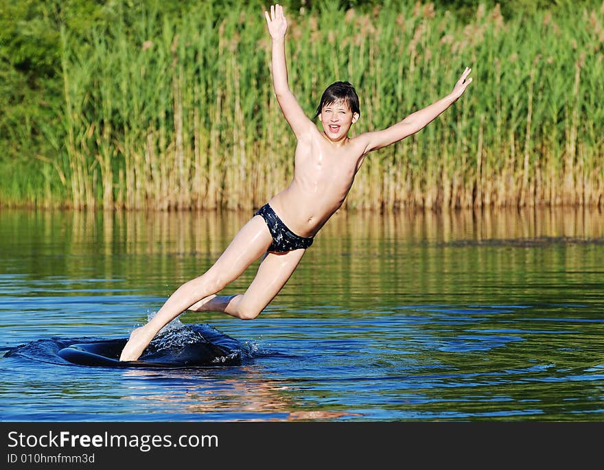 The boy is falling down off the tube to the lake water in a graceful way. The boy is falling down off the tube to the lake water in a graceful way.