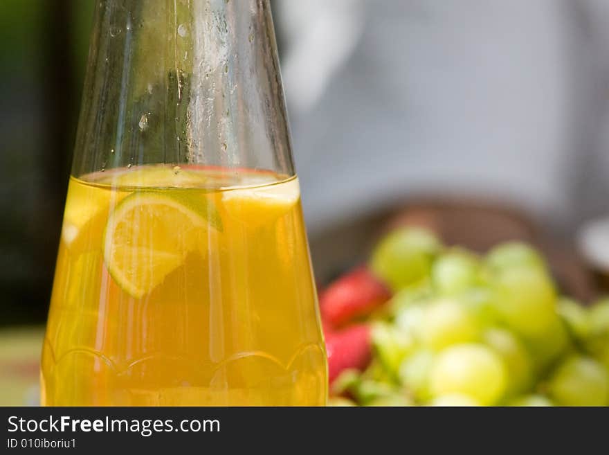 Cold jar of ice tea sits on a table with fruit in the background. Cold jar of ice tea sits on a table with fruit in the background.