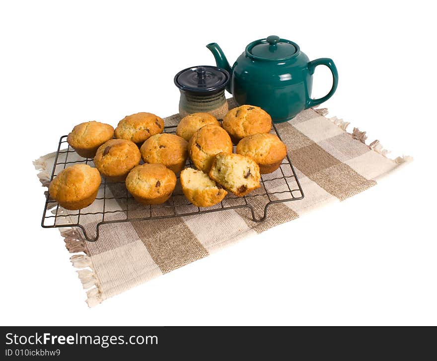 Freshly baked chocolate chip muffins on cooling rack with teapot isolated on white background.