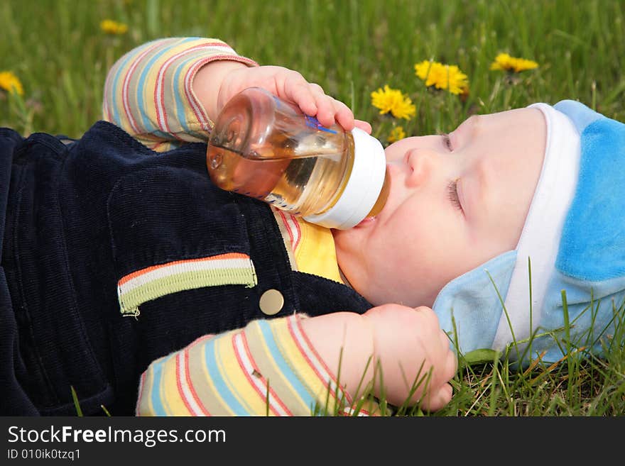 Child drinks from a bottle laying in  grass