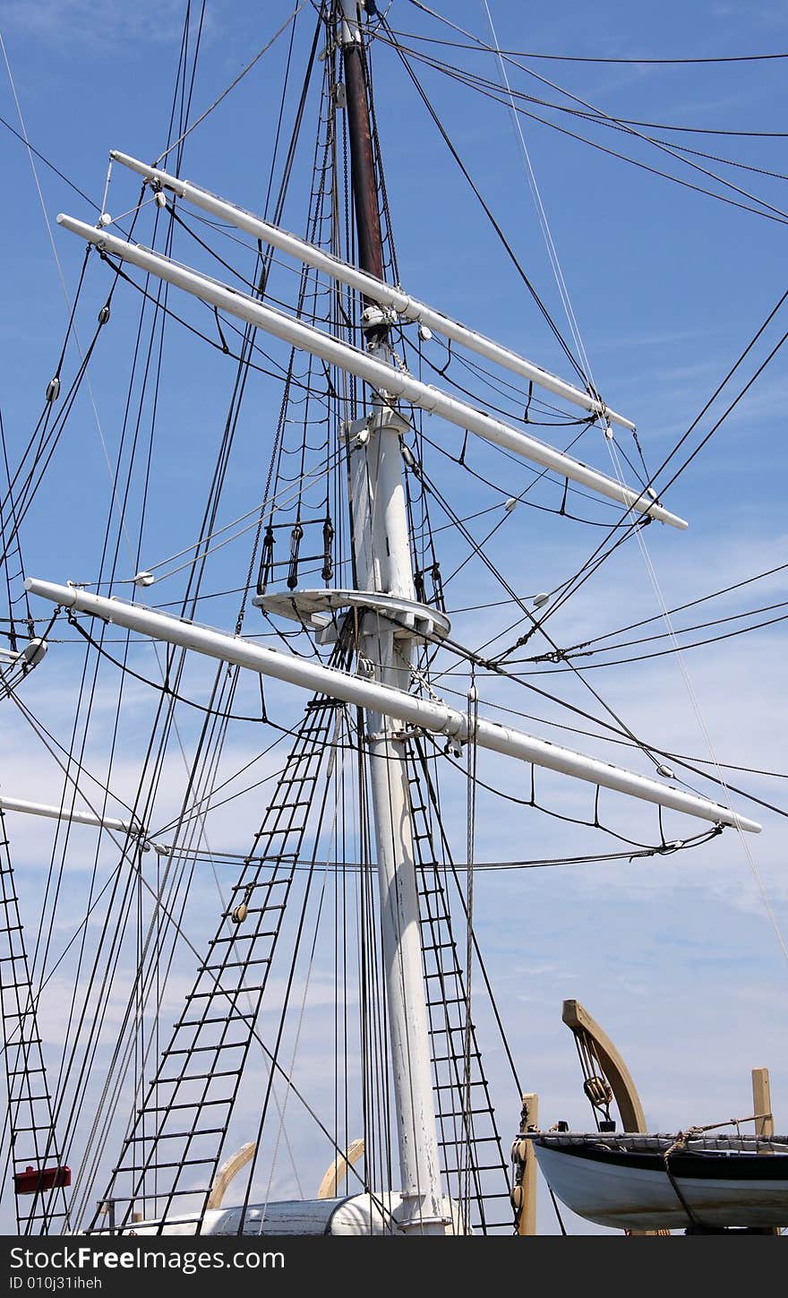 A white ship mast and life boat against a bright blue sky