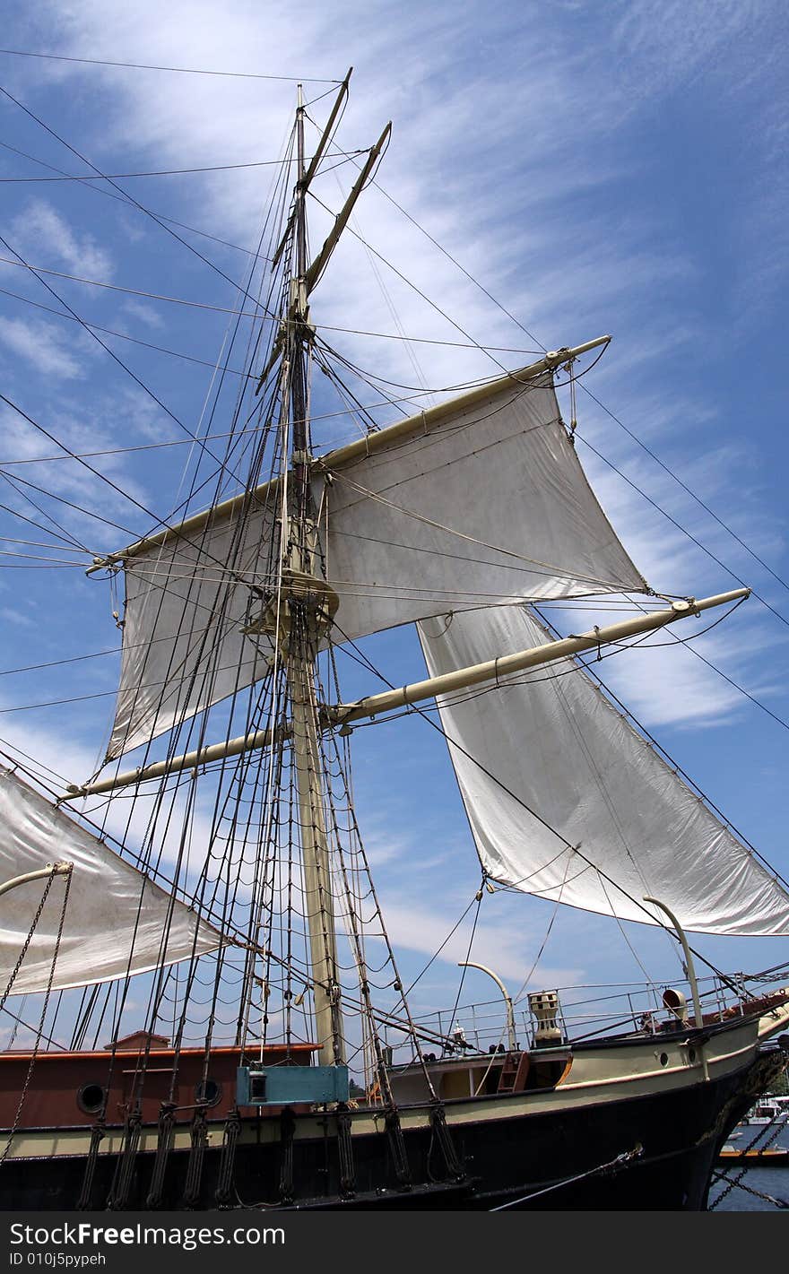 A white ship mast with sails against a bright blue sky