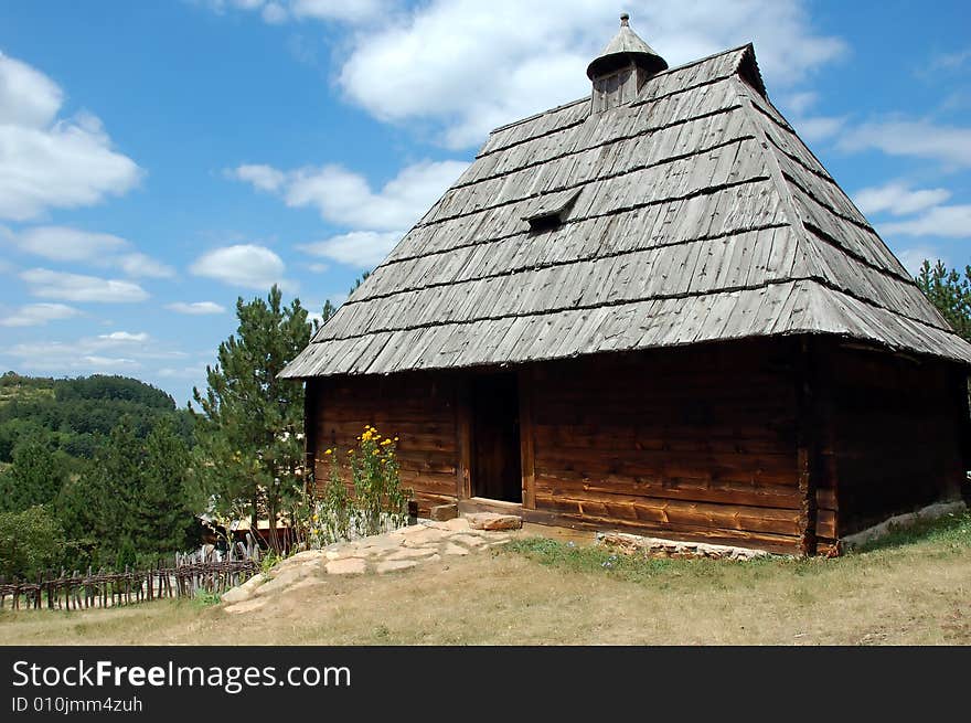 Primitive wooden country house on top of a hill with yellow flowers in front. Primitive wooden country house on top of a hill with yellow flowers in front