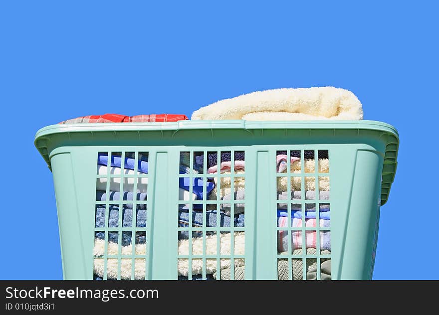 Neatly folded laundry in green plastic laundry hamper against blue background. Neatly folded laundry in green plastic laundry hamper against blue background