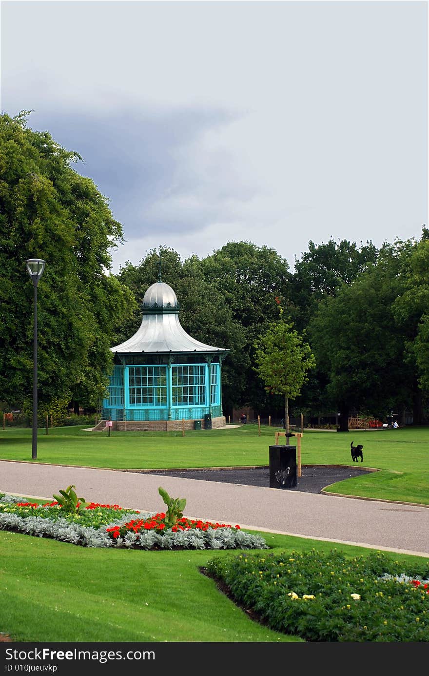 A park's green space with trees and grass, with a bandstand and a dog running with a ball. A park's green space with trees and grass, with a bandstand and a dog running with a ball.