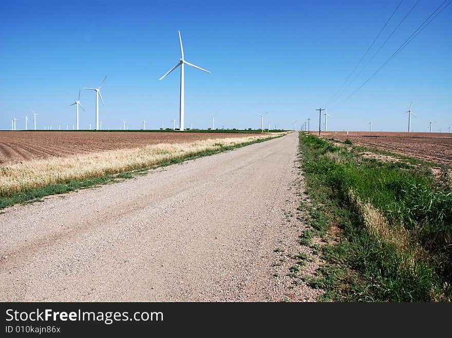 Numerous wind turbines in plowed fields with a graveled country road going through them. Numerous wind turbines in plowed fields with a graveled country road going through them