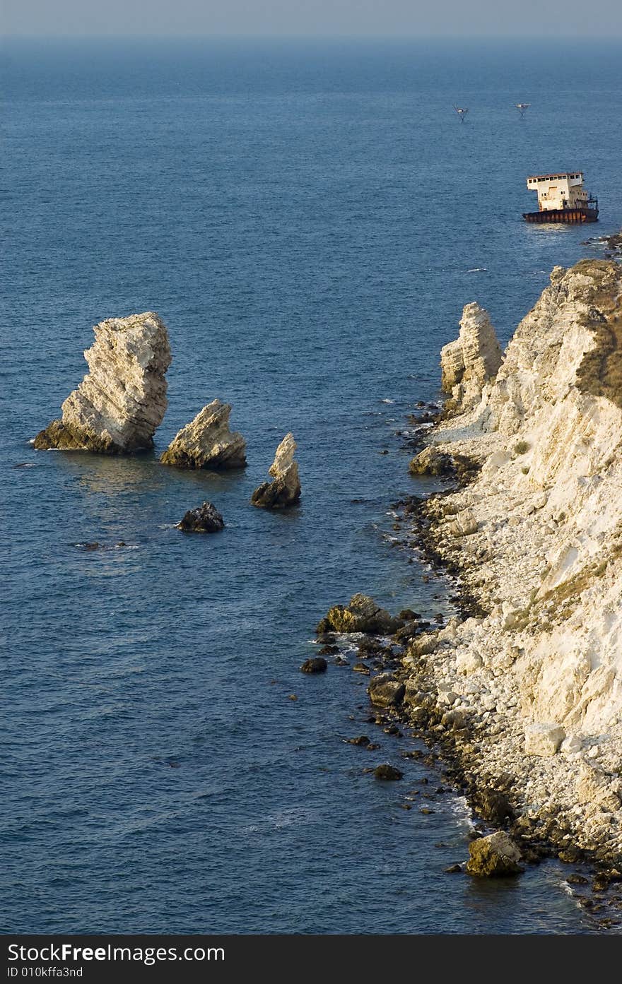 Sunset time, sunken ship sitting on the bank near the rocky coastline. Sunset time, sunken ship sitting on the bank near the rocky coastline