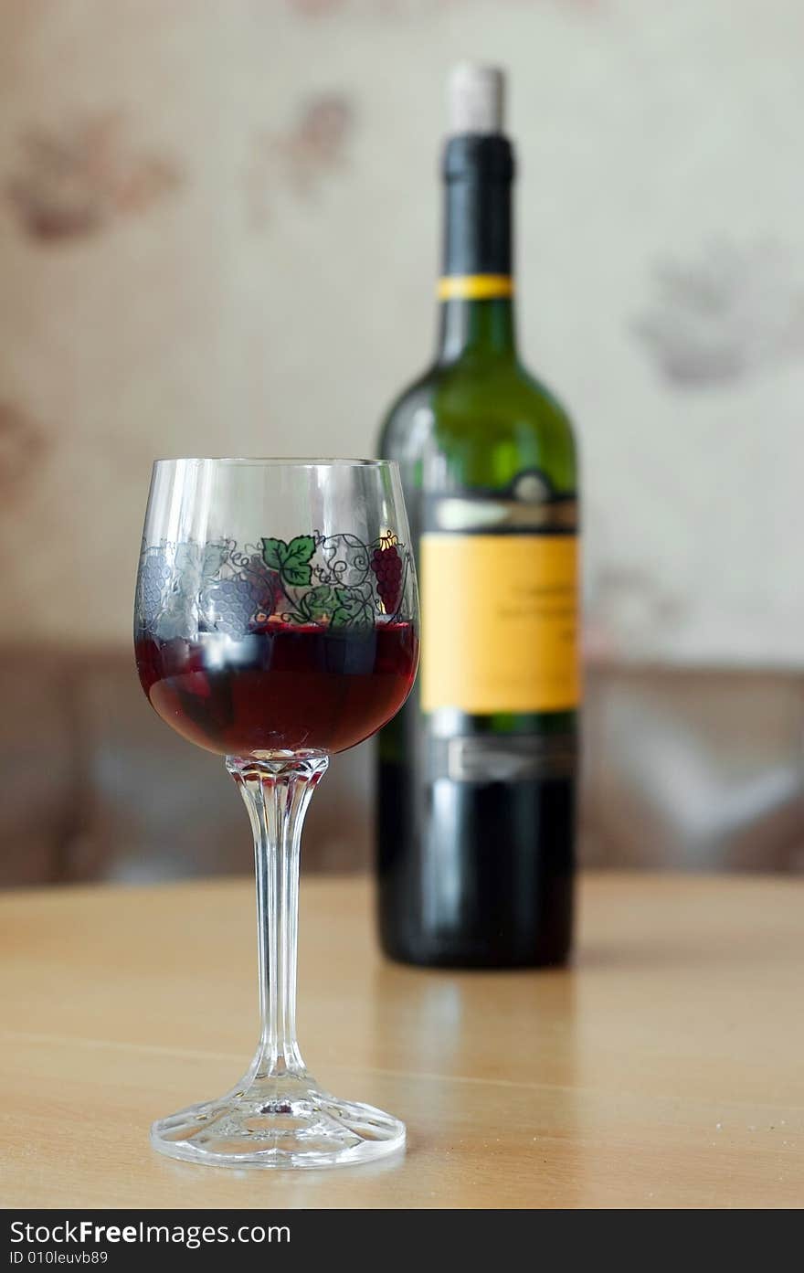 Glass with wine and wine bottle in background on table. Glass with wine and wine bottle in background on table