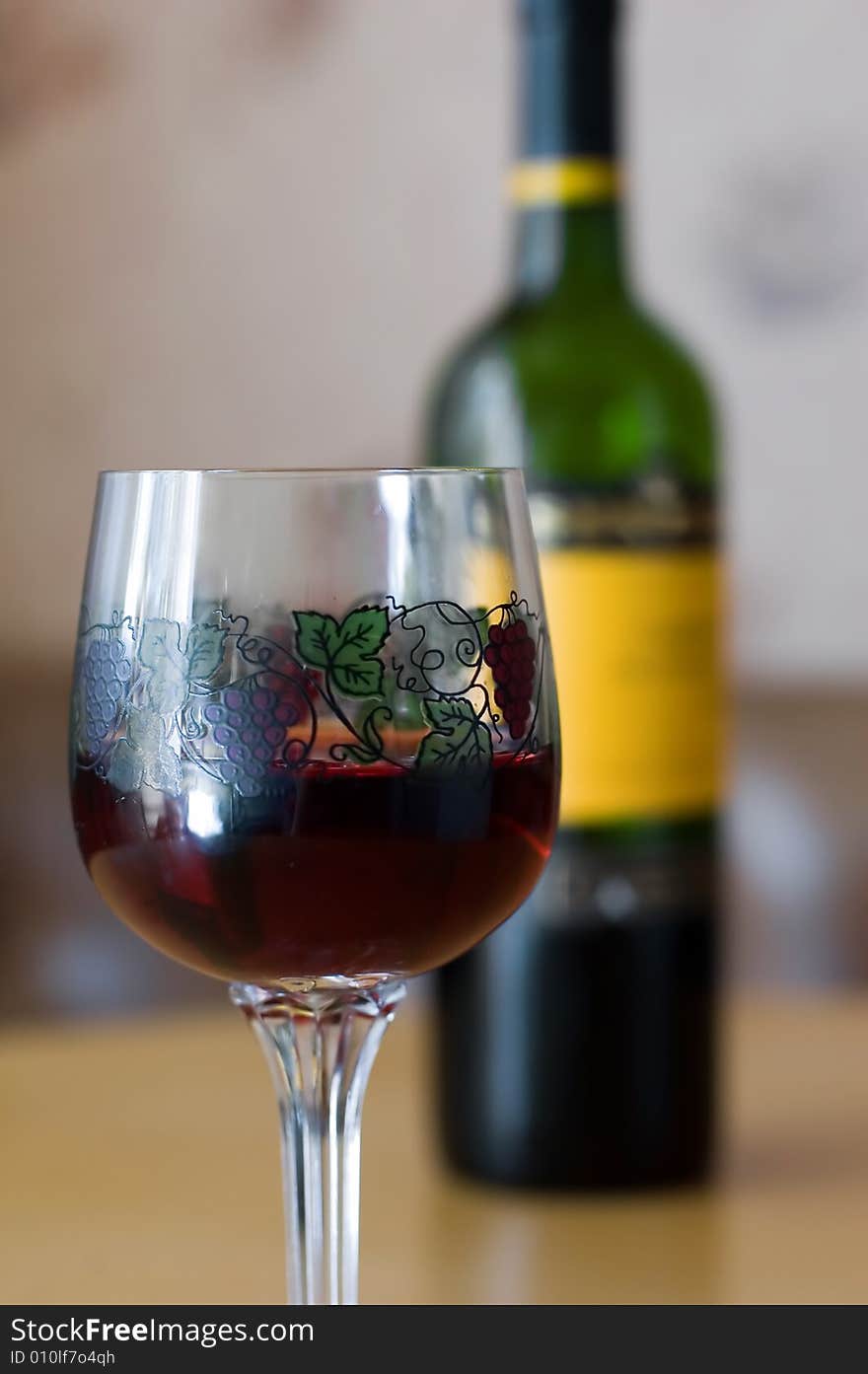 Glass with wine and wine bottle in background on table. Glass with wine and wine bottle in background on table