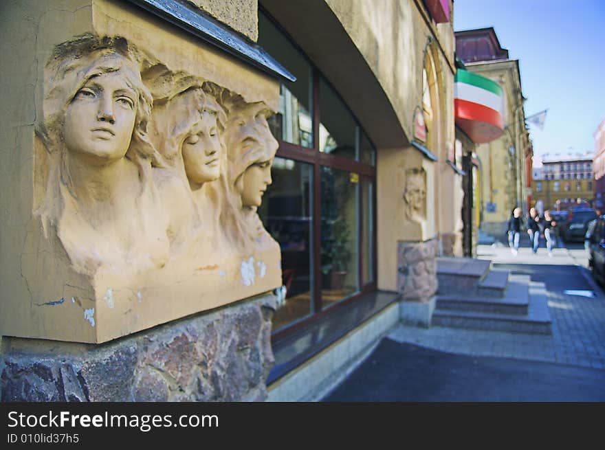 Entrance to cafe in city street with a group of people in background. The building was built before 1900, and the sculptures on the facade are public monuments and nobody can have copyright on them.