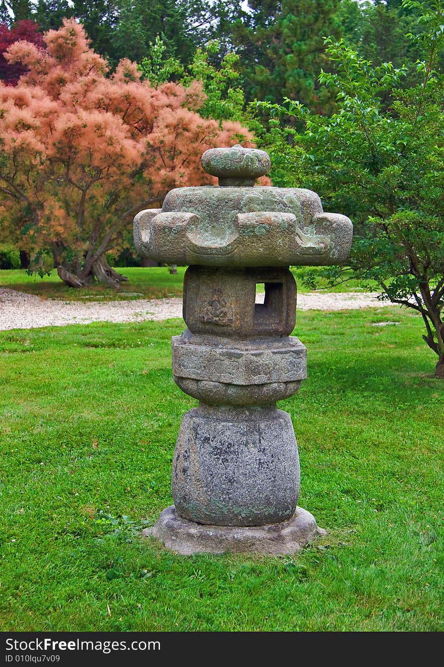 Japanese lantern in stroll garden with decorative background trees.