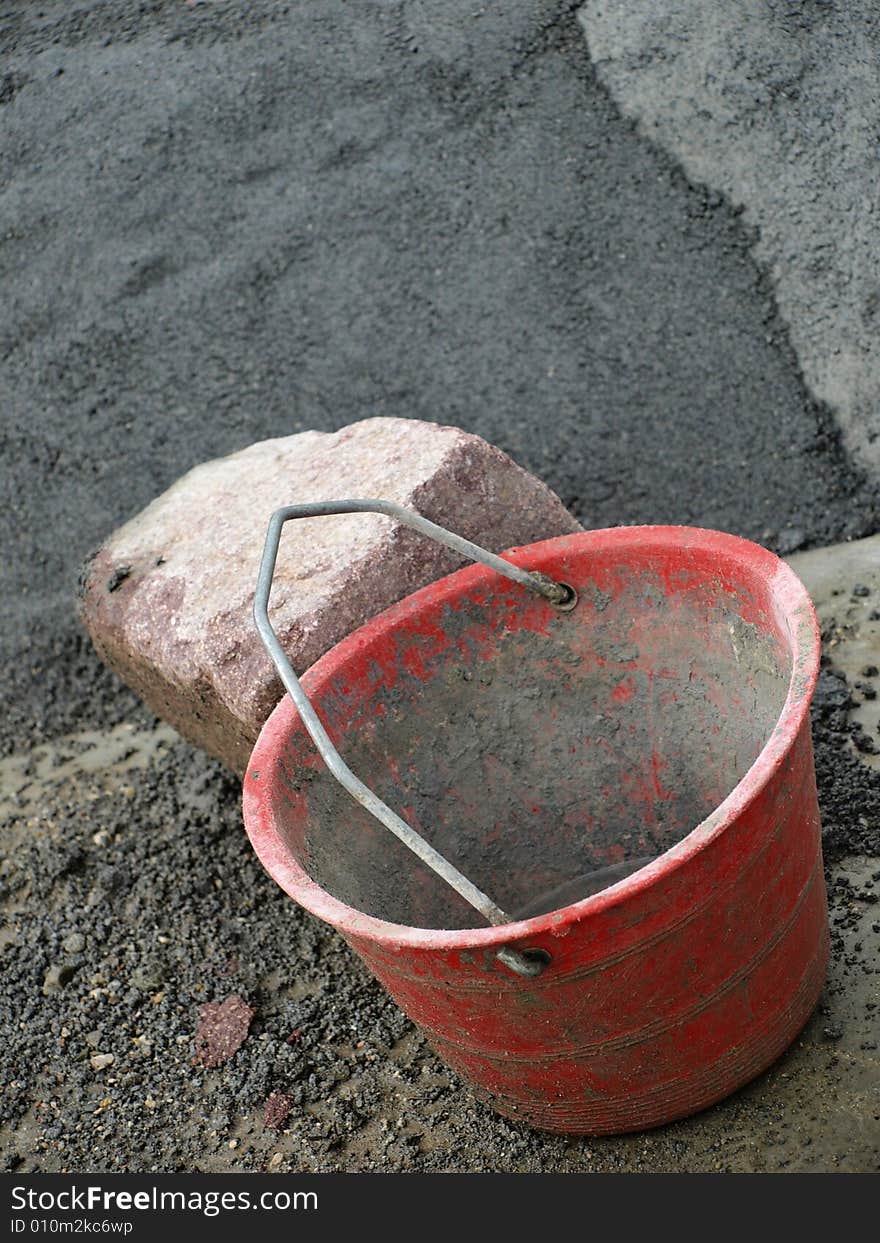 A shot of a bucket for the cement and some stones for a wall in a work place. A shot of a bucket for the cement and some stones for a wall in a work place