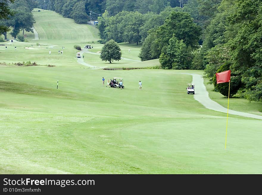 A view down a long fairway with carts and golfers. A view down a long fairway with carts and golfers