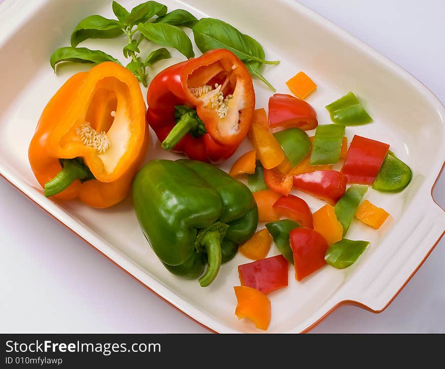 Three peppers cut in preparation in a white dish with basil leaves. Three peppers cut in preparation in a white dish with basil leaves.