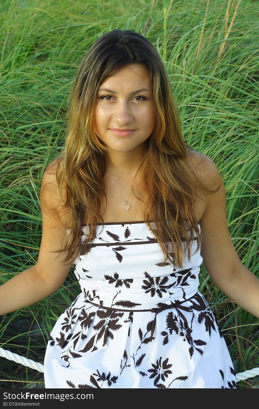 Young female sitting on a rope with green weeds in the background. Young female sitting on a rope with green weeds in the background