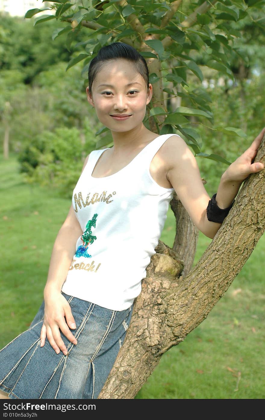 Chinese girl smiling and sitting on tree in park. Chinese girl smiling and sitting on tree in park.