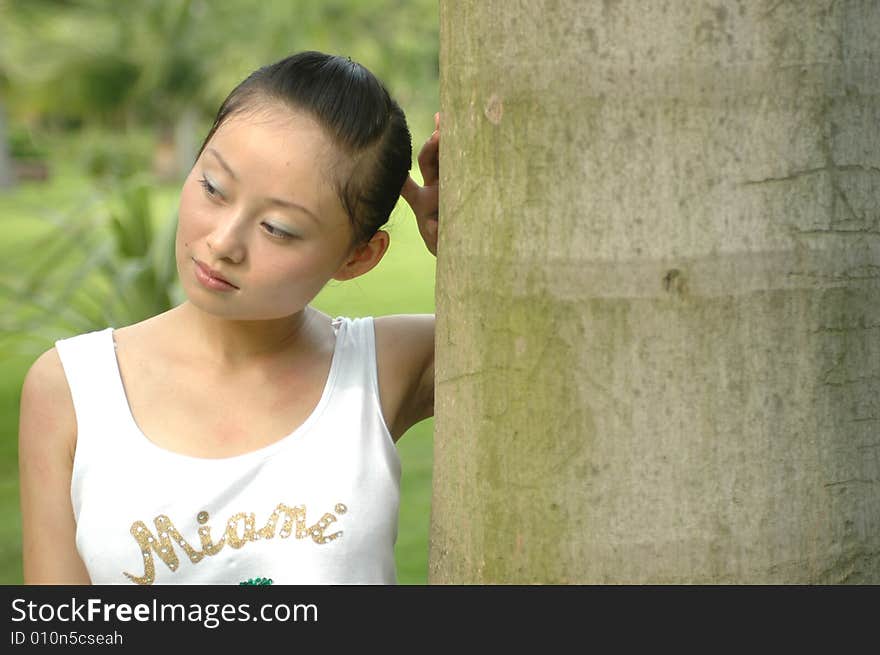 Chinese girl standing near palm tree in park, thoughtful. Chinese girl standing near palm tree in park, thoughtful.