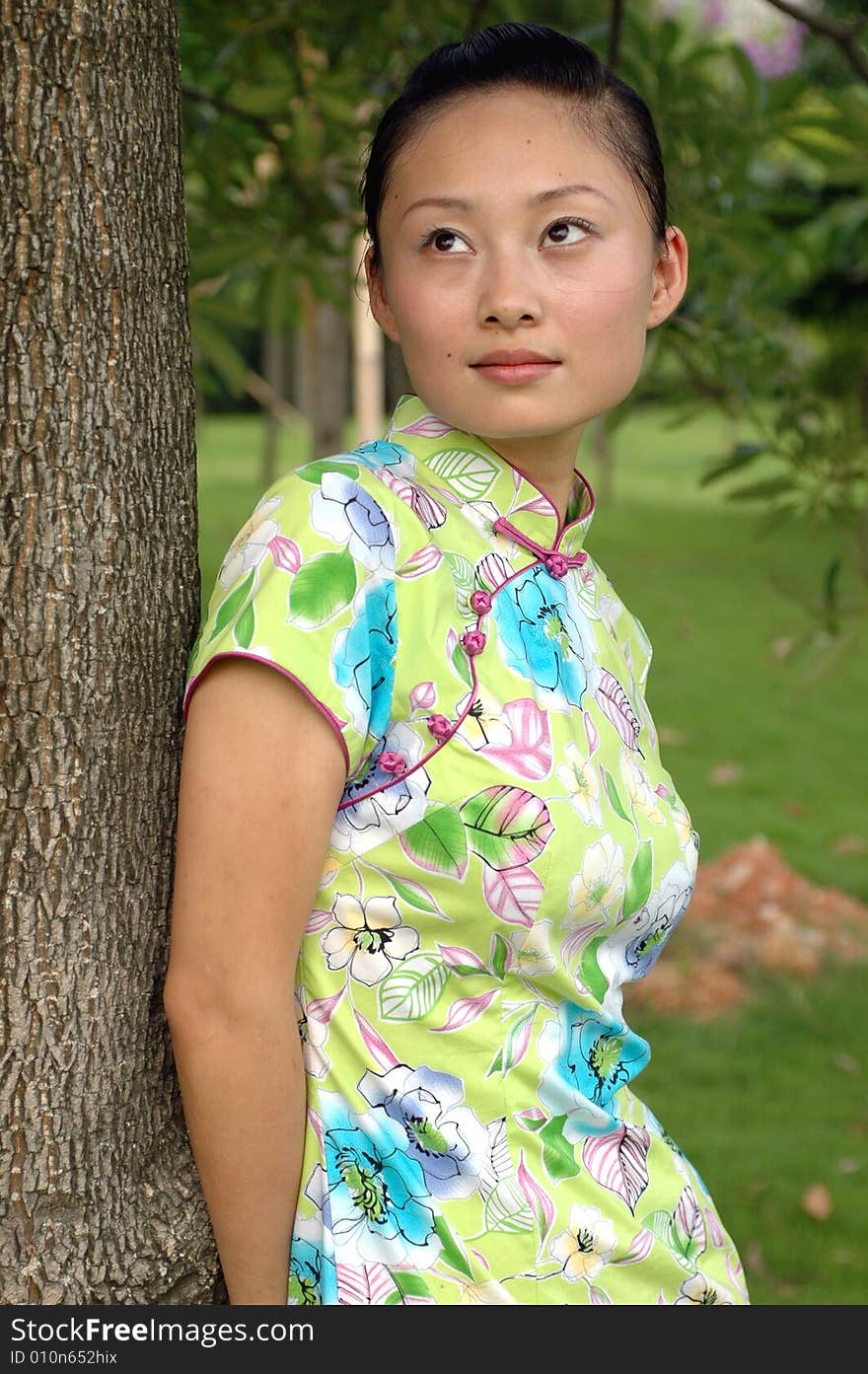 Chinese girl in traditional dress - QiPan, leaning on tree in park, thoughtful face expression. Chinese girl in traditional dress - QiPan, leaning on tree in park, thoughtful face expression.