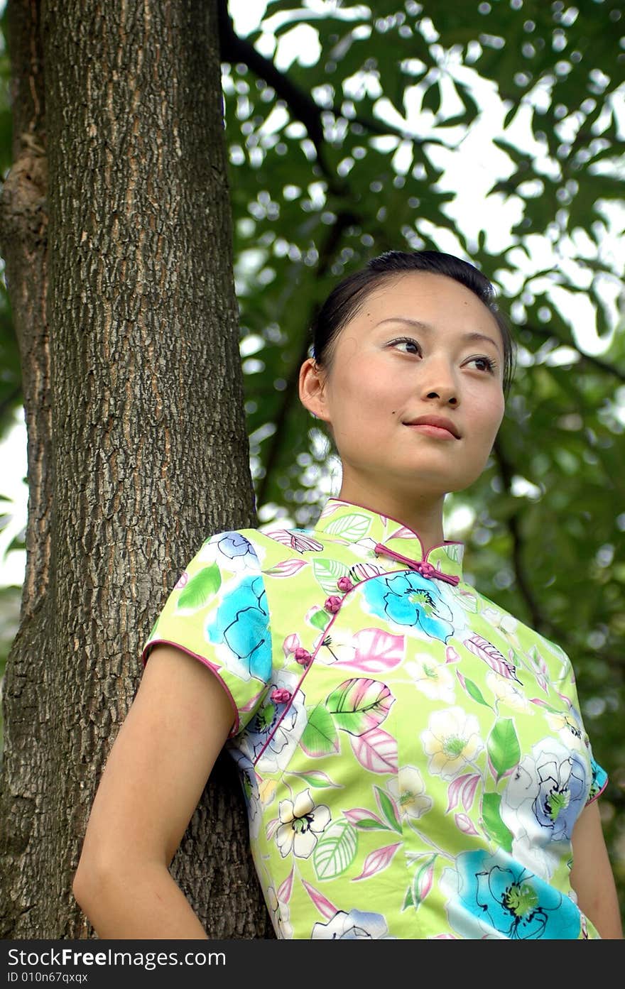 Chinese girl in traditional dress - QiPan, leaning on tree in park, thoughtful face expression. Chinese girl in traditional dress - QiPan, leaning on tree in park, thoughtful face expression.