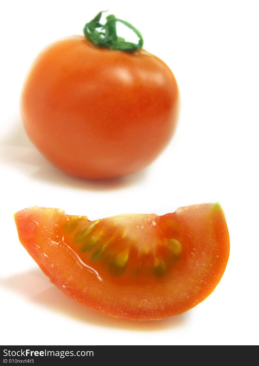 A slice of tomato and a blurred whole one isolated on white background. A slice of tomato and a blurred whole one isolated on white background