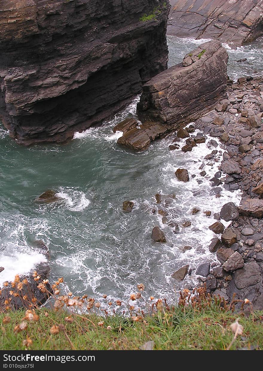 Looking down from the cliff top the waves are swirling around the rocks.  A large dark rock looms upward.  Do you have vertigo or a good head for heights? On the coast, sea cliffs can be dangerous.