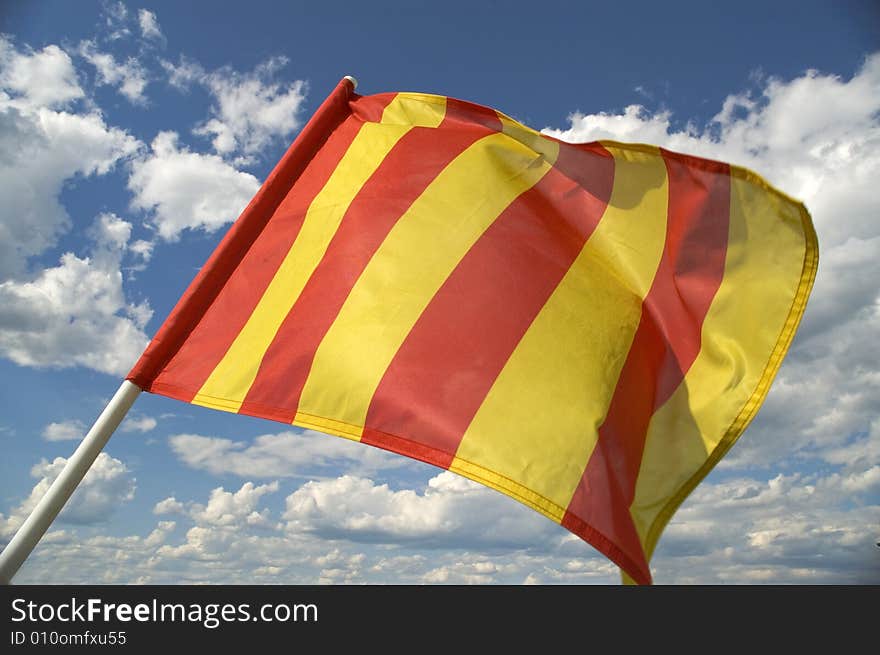 The orange striped flag on a background of the dark blue sky with clouds is yellow. The orange striped flag on a background of the dark blue sky with clouds is yellow.