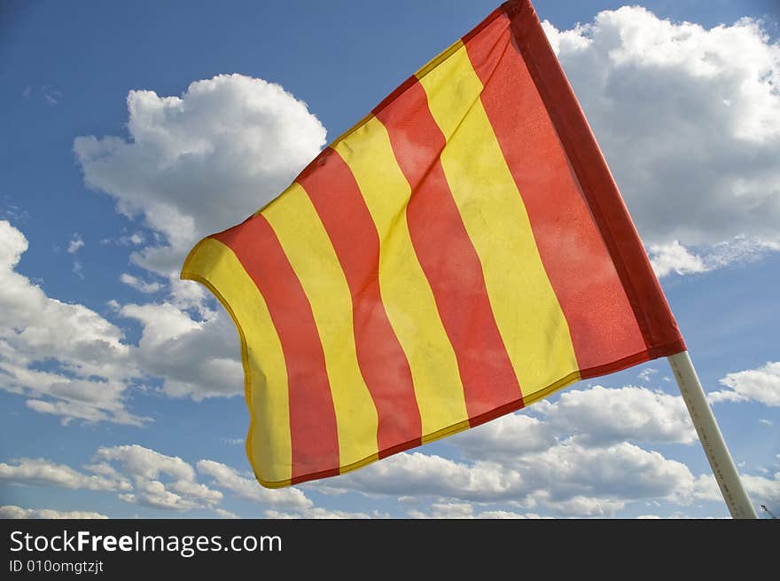 The orange striped flag on a background of the dark blue sky with clouds is yellow. The orange striped flag on a background of the dark blue sky with clouds is yellow.
