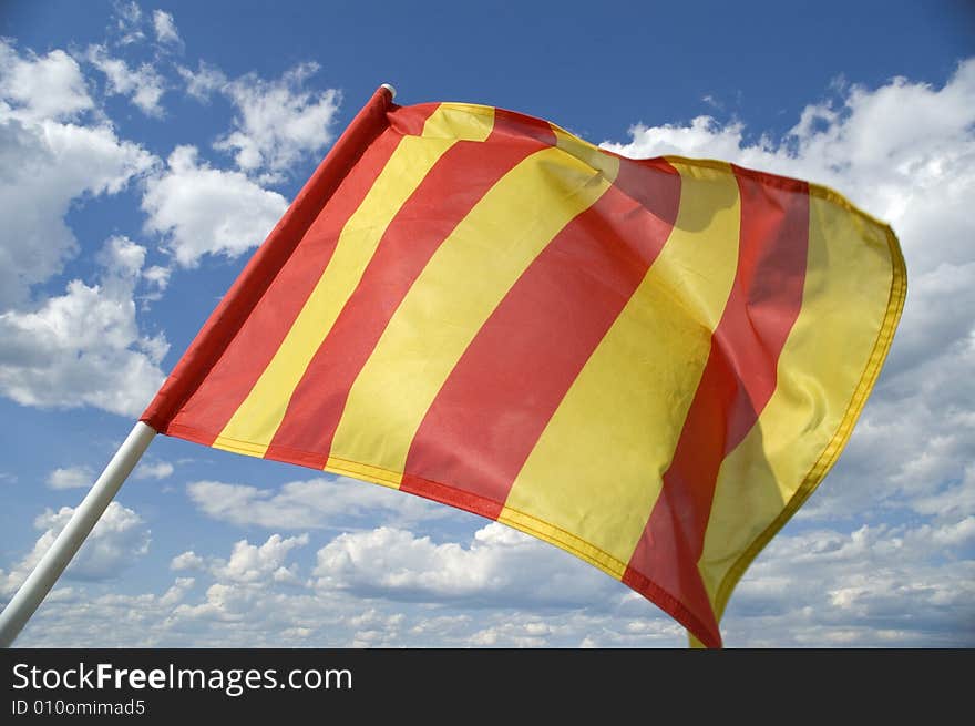 The orange striped flag on a background of the dark blue sky with clouds is yellow . The orange striped flag on a background of the dark blue sky with clouds is yellow .