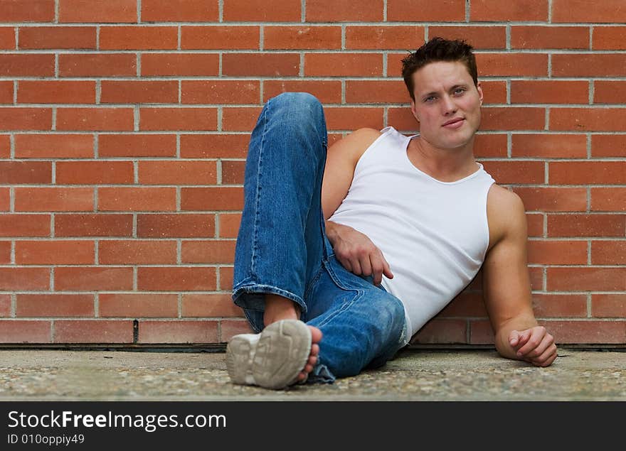 A fit male model leaning against a brick wall. A fit male model leaning against a brick wall