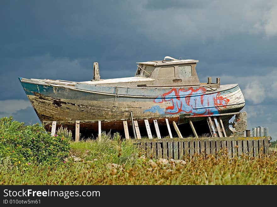 Vintage and leaky boat on land under dark and heavy skies