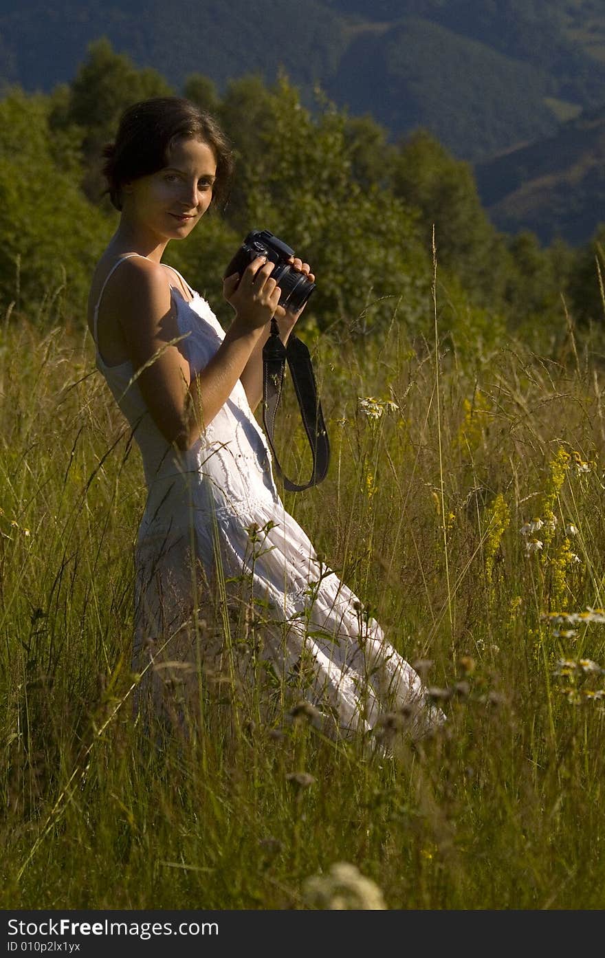 Woman in white holding a camera in the middle of the mountains