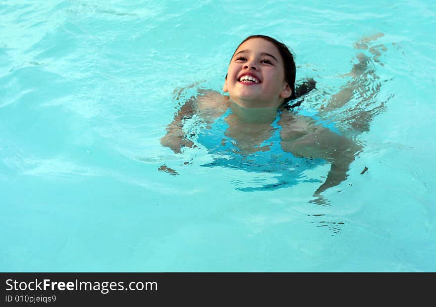 A smiling, tanned 6-year-old girl floats in a swimming pool. She has big brown eyes and brown hair and is of Asian and Caucasian background, multi-racial. A smiling, tanned 6-year-old girl floats in a swimming pool. She has big brown eyes and brown hair and is of Asian and Caucasian background, multi-racial