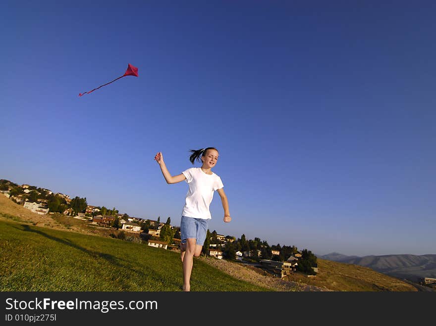 Girl running and flying a kite in a park with blue sky