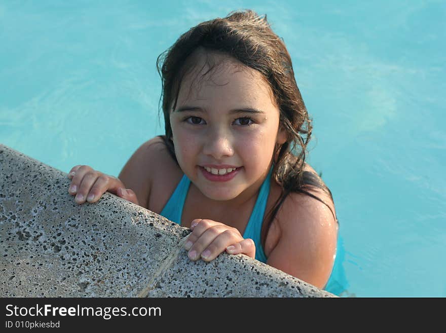 A smiling 6-year-old girl holds onto the edge of a swimming pool. She has big brown eyes and brown hair and is of Asian and Caucasian background, multi-racial. A smiling 6-year-old girl holds onto the edge of a swimming pool. She has big brown eyes and brown hair and is of Asian and Caucasian background, multi-racial.