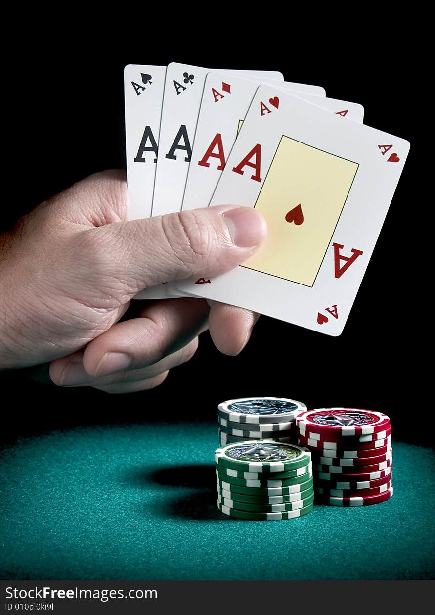 A man's hand holding four aces over three piles of different colors chips on a green felt.