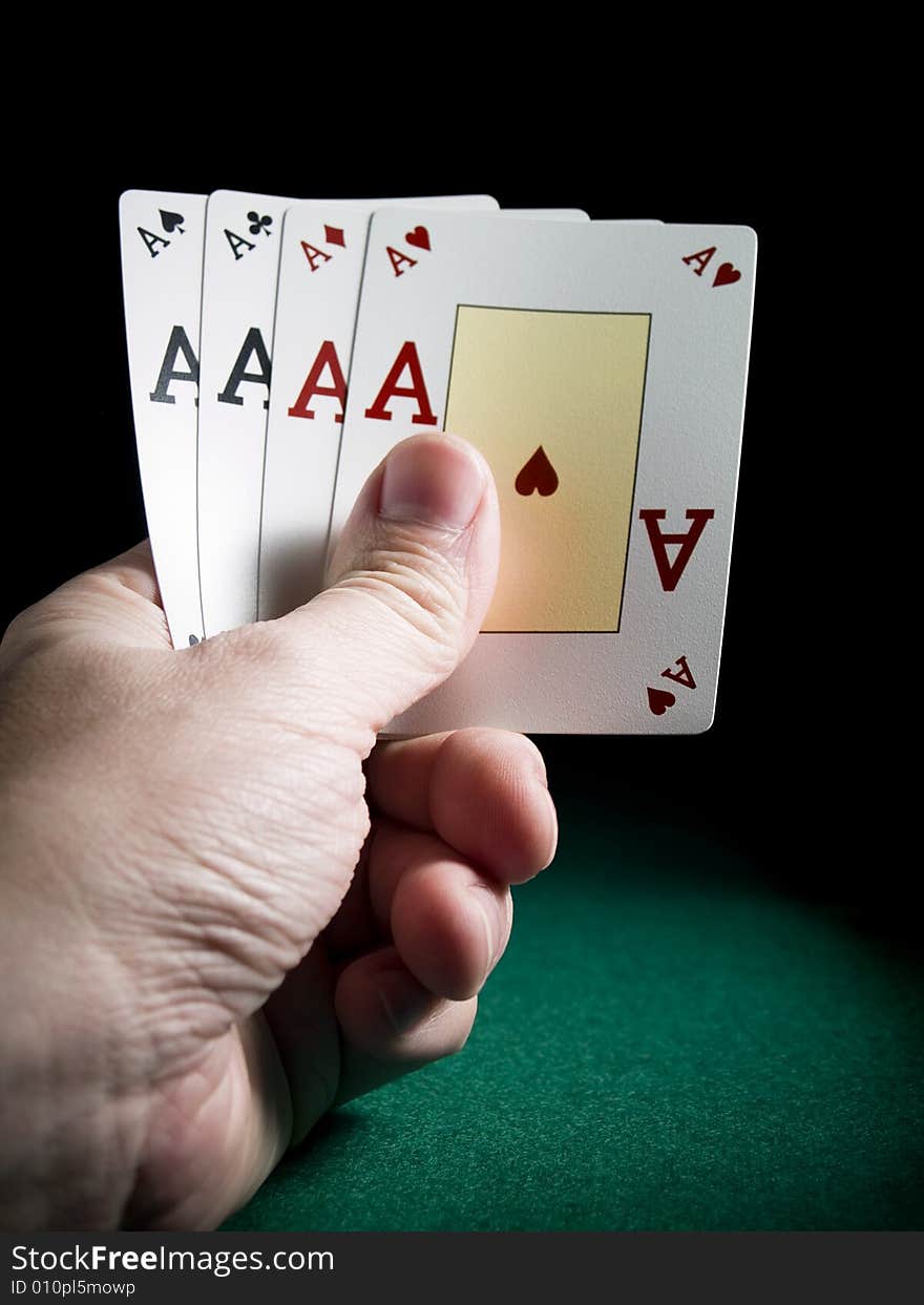 A man's hand holding four aces over a green felt.