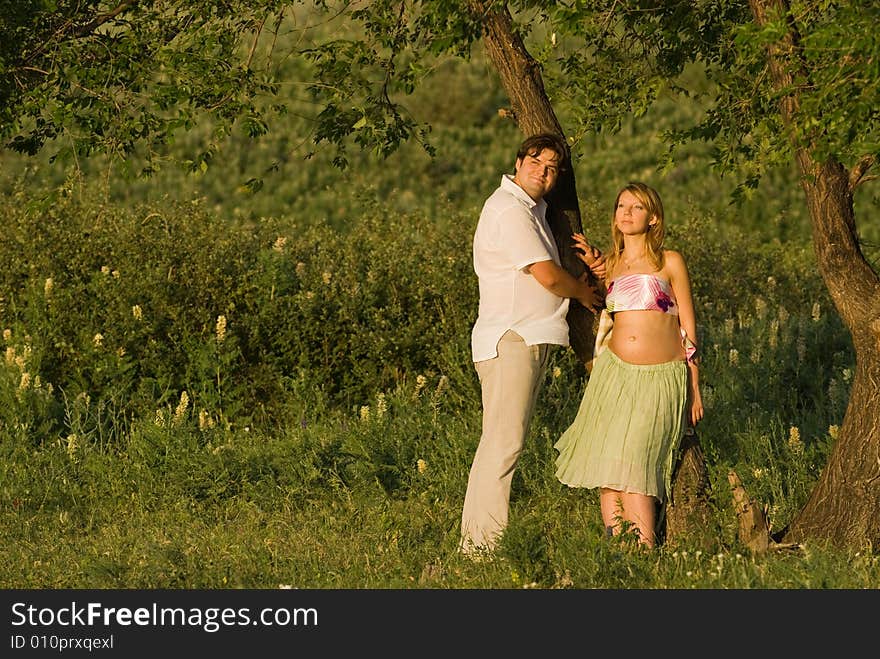 Young happy couple outdoors at a sunset, woman is pregnant