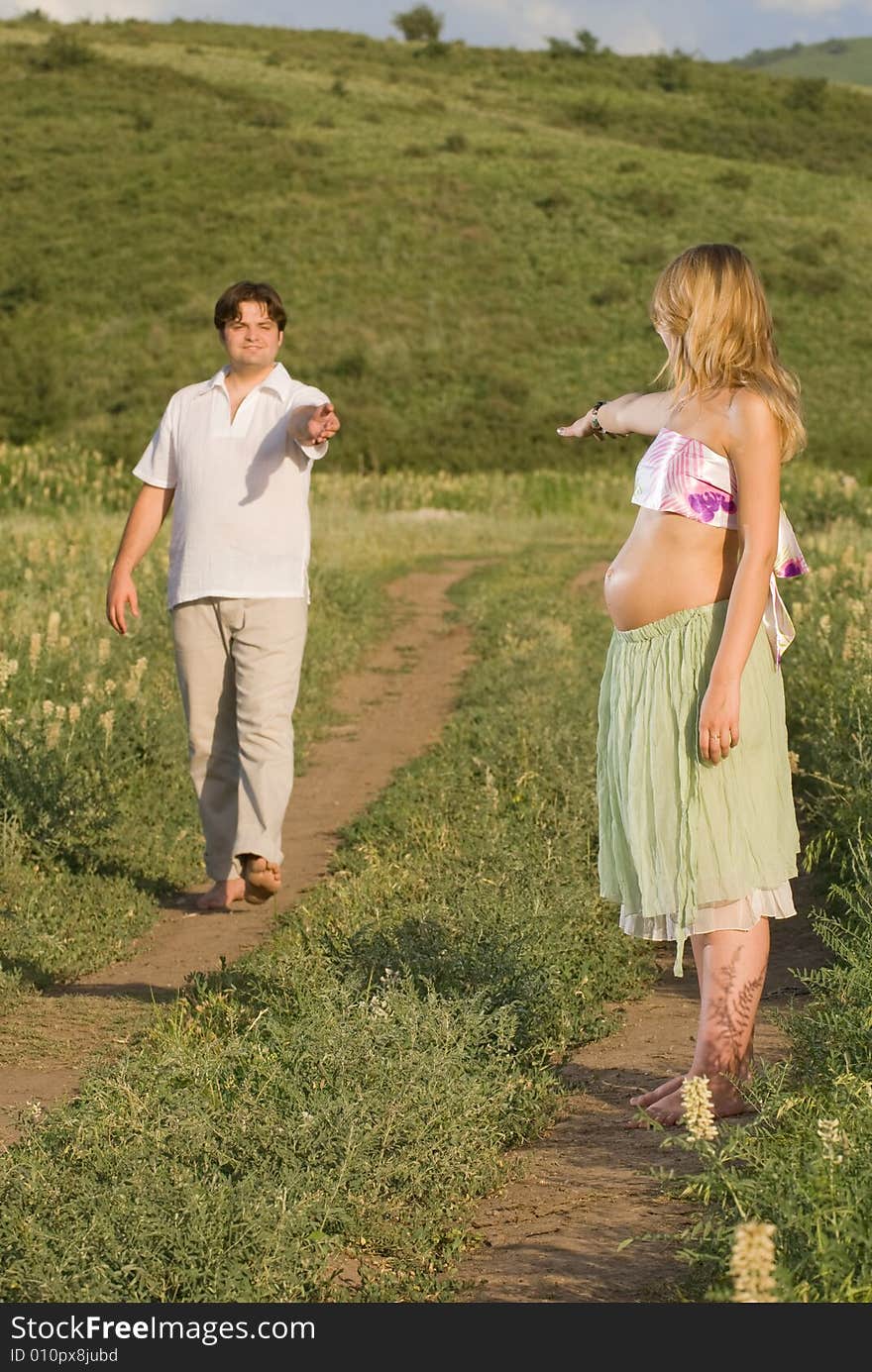 Young married couple on the walk, woman is pregnant and gives her hand to her husband. Young married couple on the walk, woman is pregnant and gives her hand to her husband