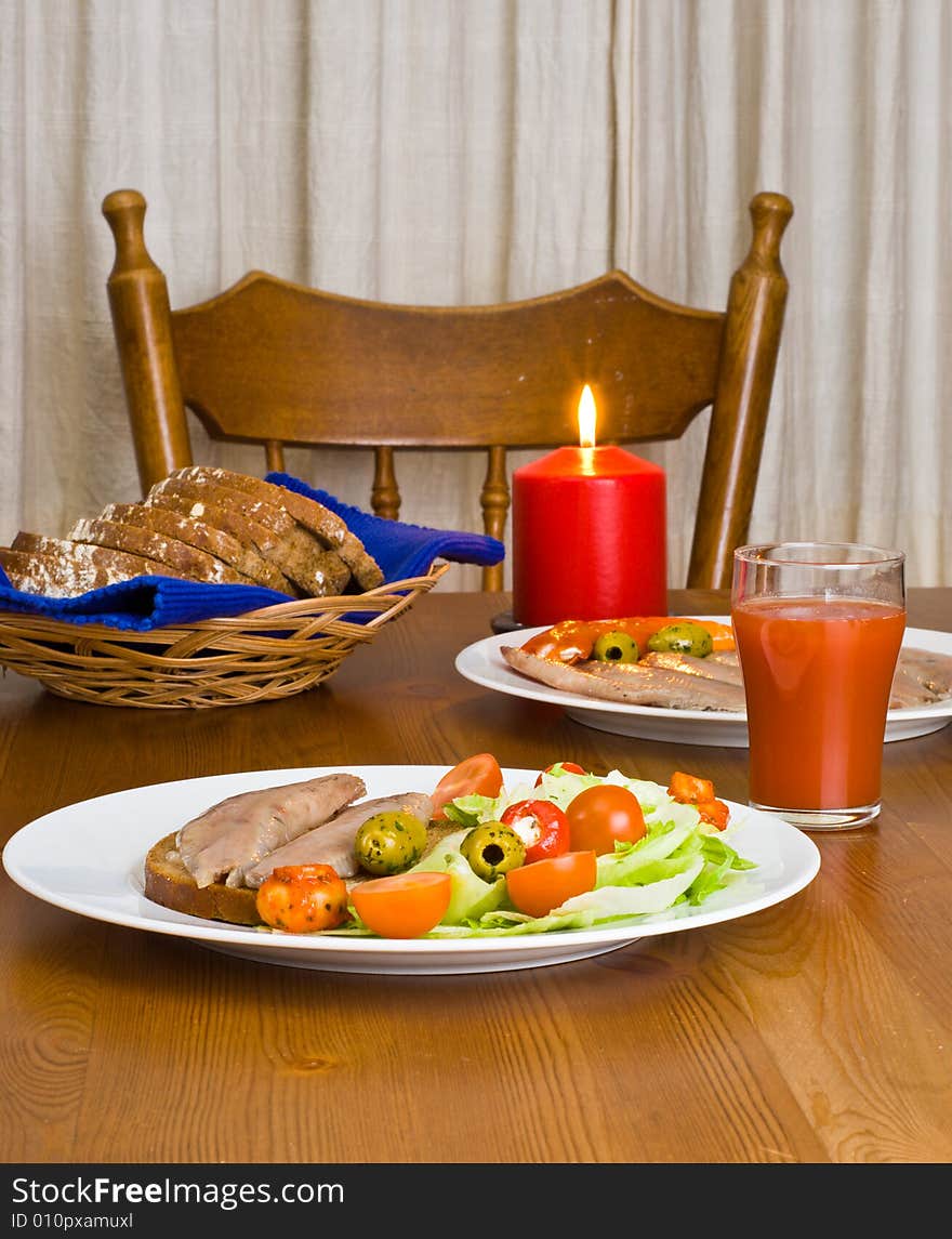 Table served with herring with salad, bread and tomato juice. Burning candle. Table served with herring with salad, bread and tomato juice. Burning candle.