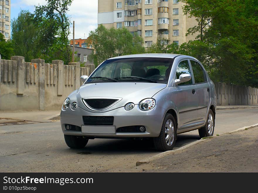 Silvery car stand at road near fence