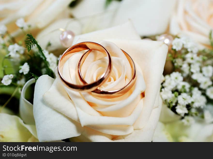 Two rings lie on roses bud on wedding bouquet background. macro