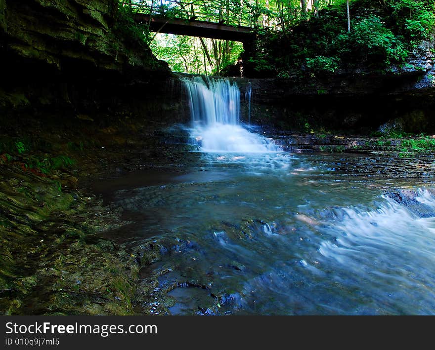 This is a small water fall with a bridge overhead.