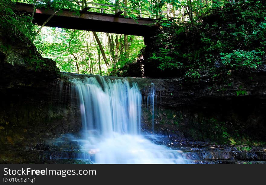 This is a small water fall with a bridge overhead.