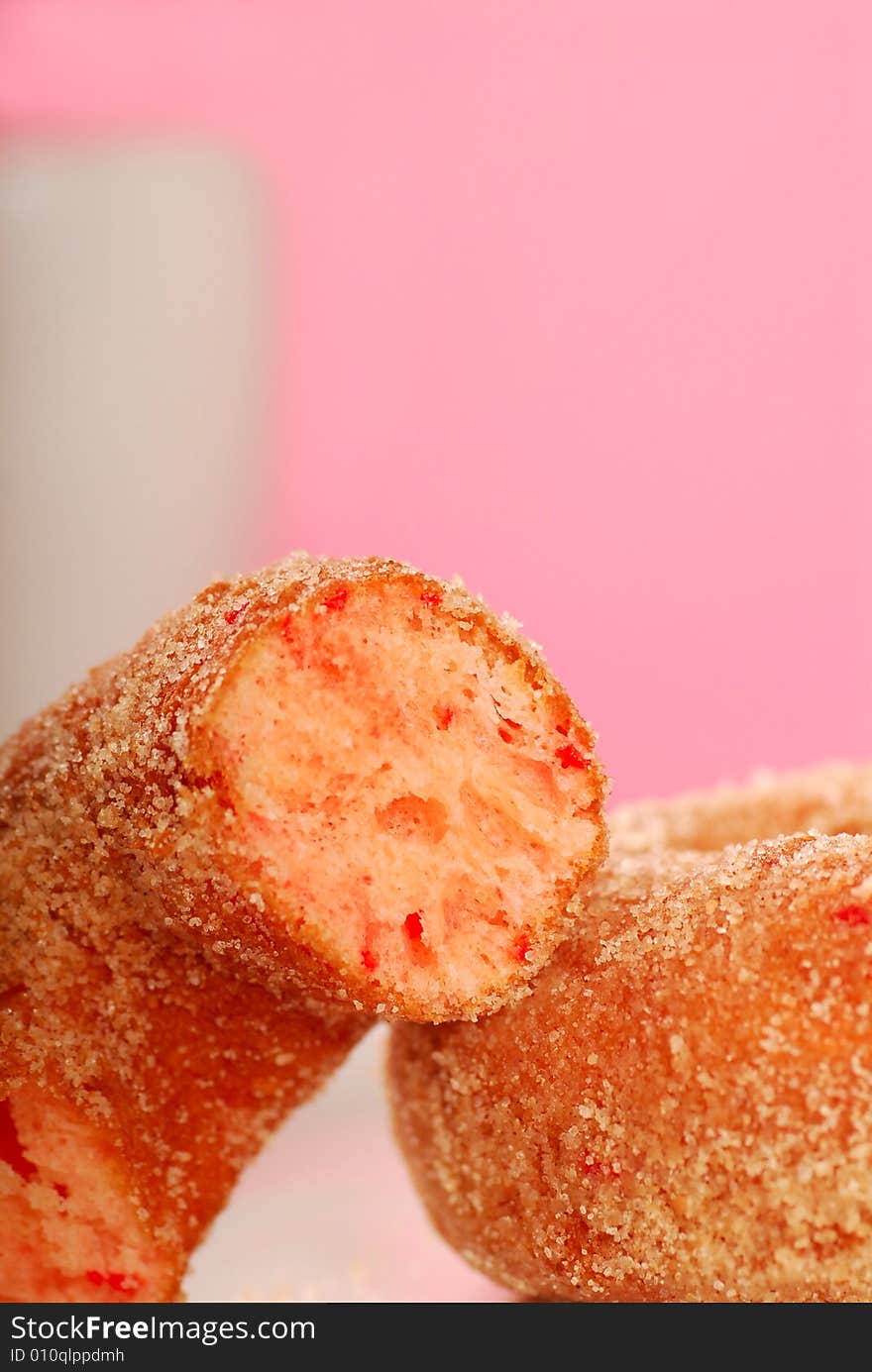 Two freshly made strawberry doughnuts with a cup of coffee in the background