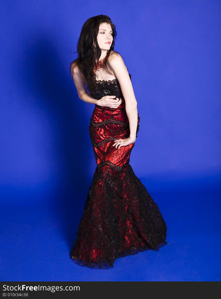 Beautiful young woman wearing a red evening gown in front of a blue background