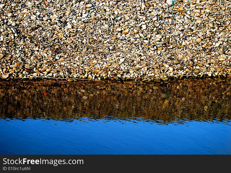 Bank of stones reflecting in a clear blue river. Bank of stones reflecting in a clear blue river