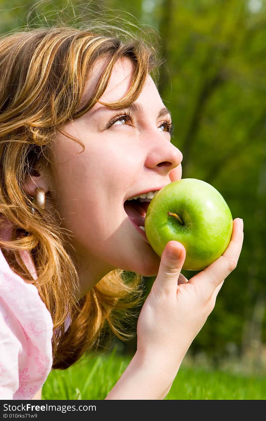 Pretty woman eating green apple on the summer glade