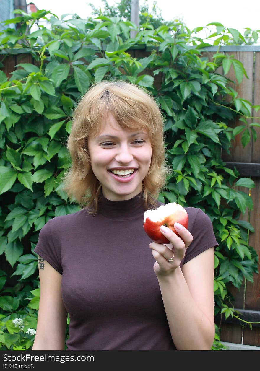 The young smiling girl with red apple on a background of wild grapes. The young smiling girl with red apple on a background of wild grapes.