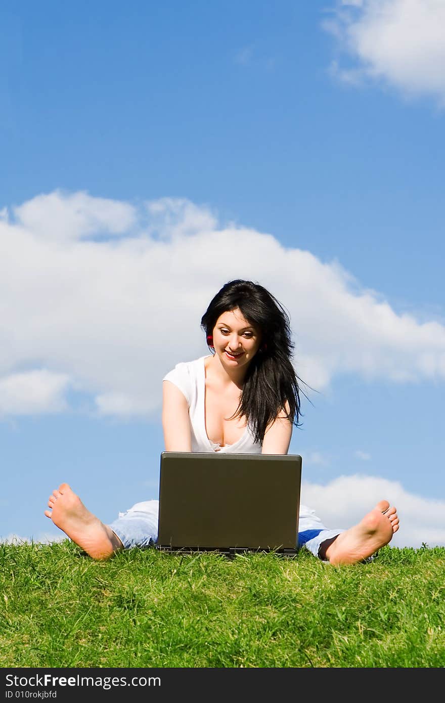 Pretty woman with laptop on the green grass