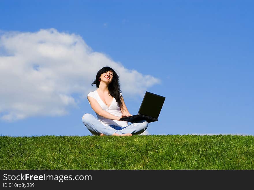 Pretty woman with laptop on the green grass